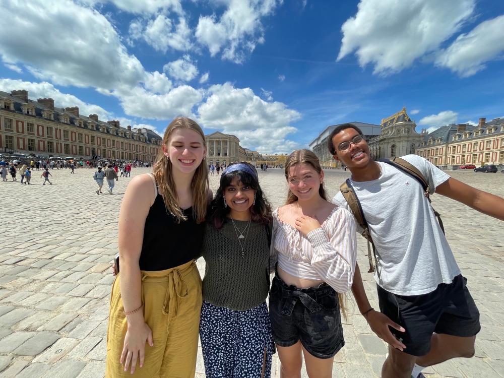 Three women and one man standing outside the Palace of Versailles on a sunny day